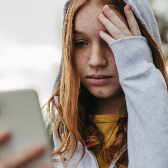 Mädchen mit Smartphone, das sich an den Kopf fasst und besorgt aussieht