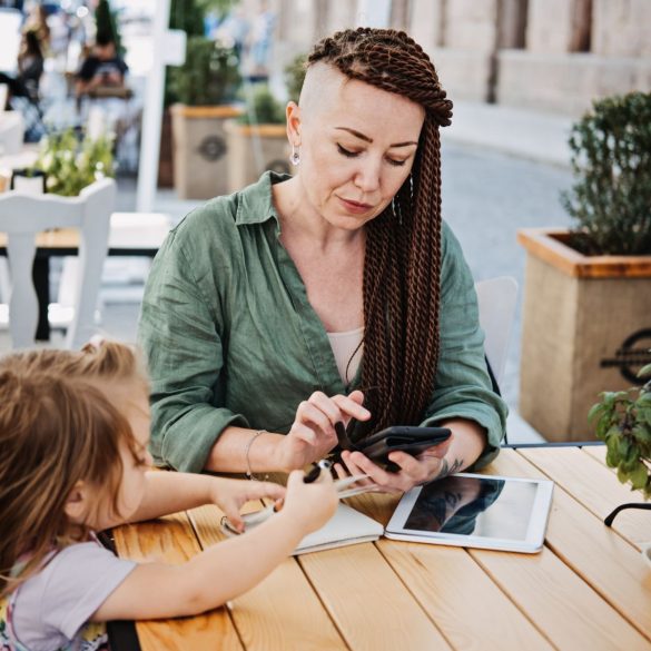 Frau mit Kind tippt auf ihrem Smartphone.